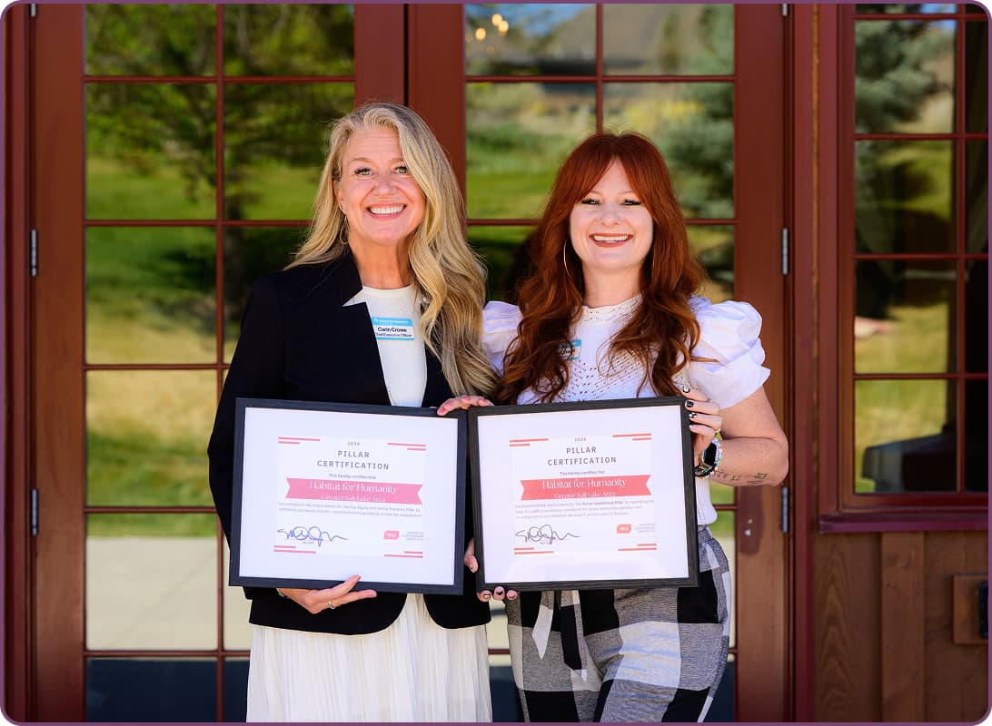 Two women holding framed Pillar Certification awards presented to Habitat for Humanity Greater Salt Lake Area